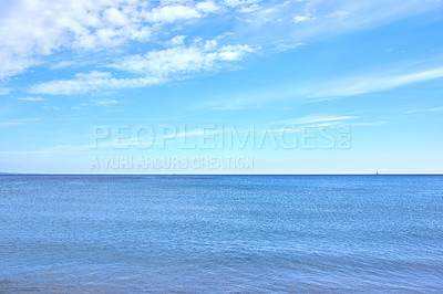 Buy stock photo Copy space at sea with a cloudy blue sky background. Calm ocean waves at an empty beach with a sailboat cruising in the horizon. Scenic and picturesque landscape view for a peaceful summer holiday
