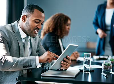 Buy stock photo Cropped shot of a handsome young businessman working on his tablet during a meeting in the boardroom