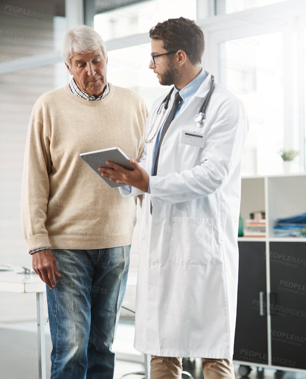 Buy stock photo Cropped shot of a young male doctor showing his senior male patient something on a digital tablet