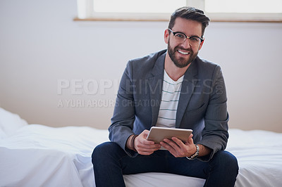 Buy stock photo Cropped portrait of a handsome young businessman working on a tablet while sitting on his bed at home