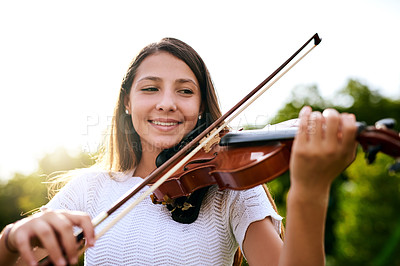 Buy stock photo Shot of a cheerful young girl playing the violin while standing in the backyard of her home during the day