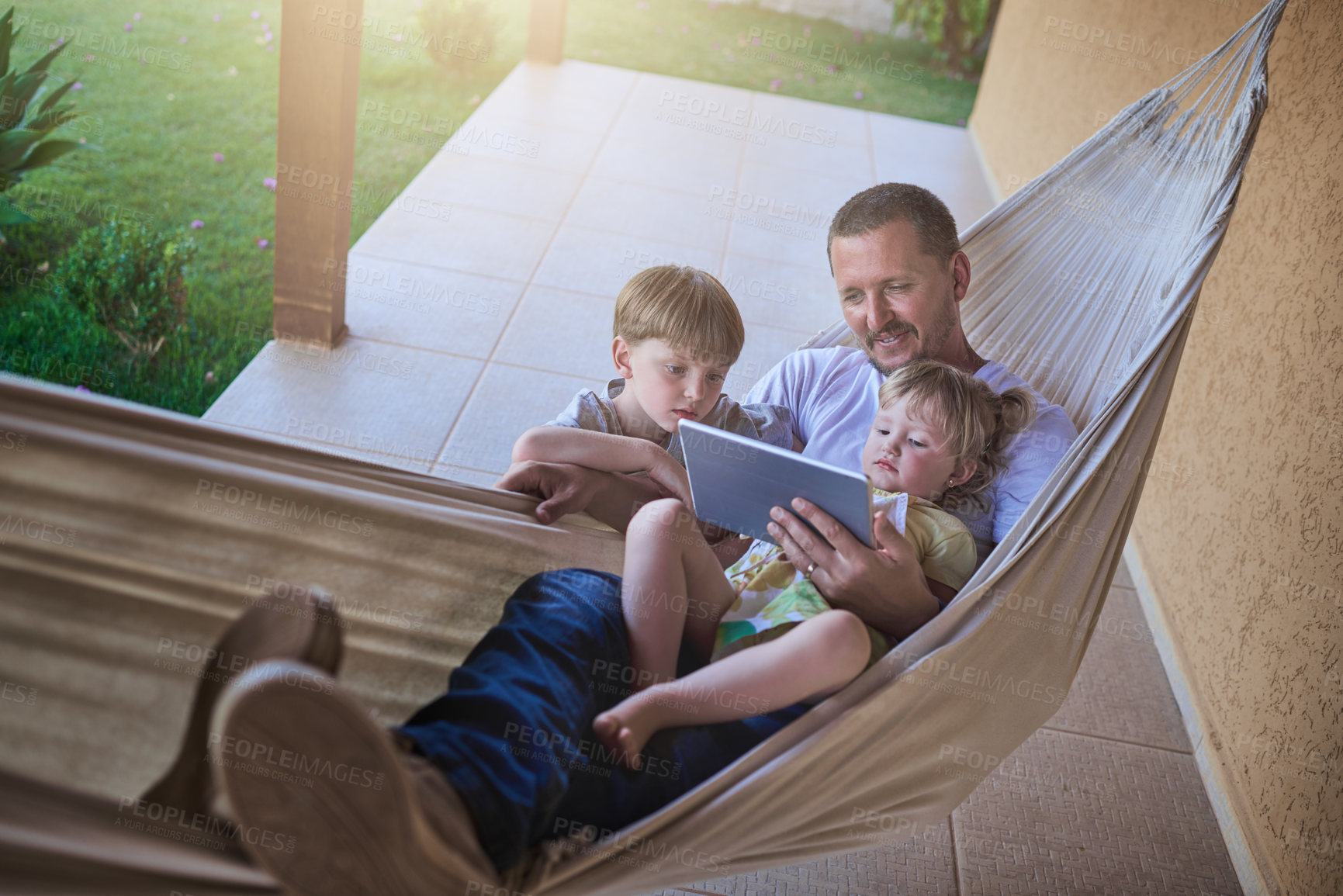 Buy stock photo Shot of a father and his two little children using a digital tablet while relaxing on a hammock outdoors