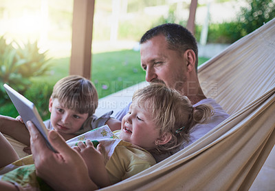 Buy stock photo Shot of a father and his two little children using a digital tablet while relaxing on a hammock outdoors