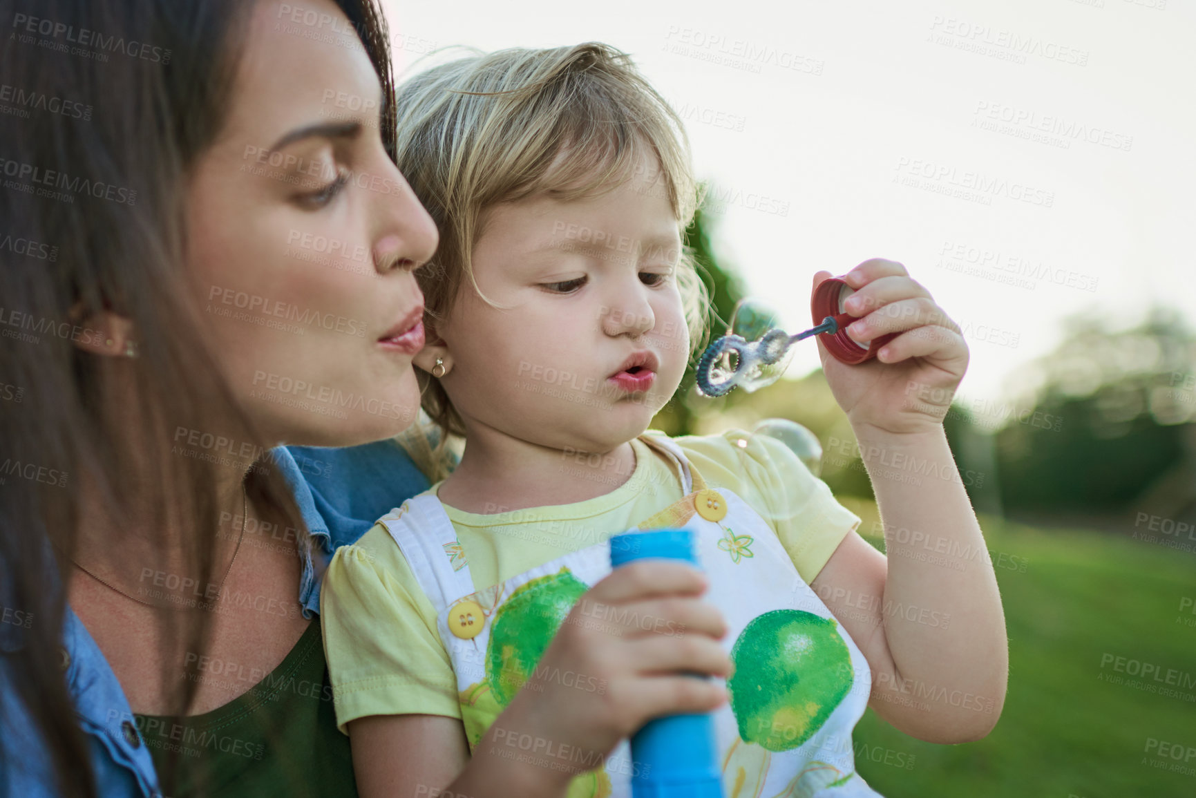 Buy stock photo Shot of a mother and her little daughter blowing bubbles outdoors