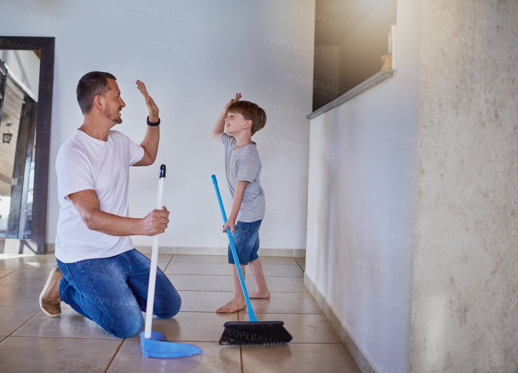 Buy stock photo Shot of a father and his little son high fiving each other while sweeping the floor at home