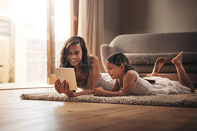 Buy stock photo Shot of a young woman and her adorable daughter using a digital tablet while relaxing on the floor at home