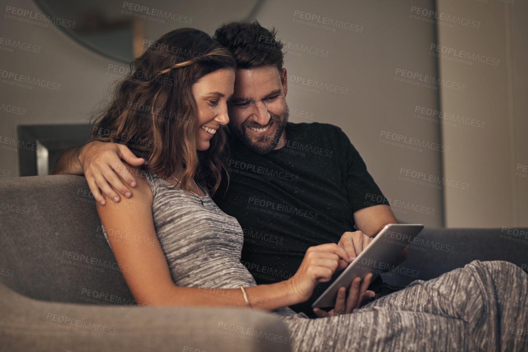 Buy stock photo Shot of a young couple using a digital tablet together while relaxing on the sofa at home