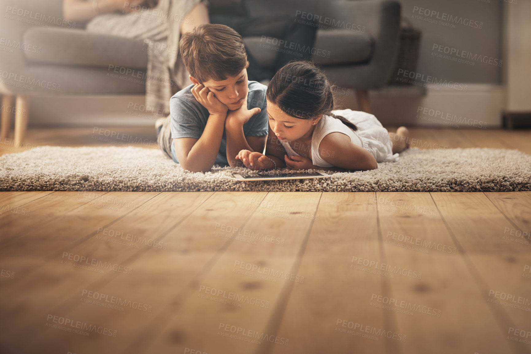Buy stock photo Shot of an adorable brother and sister using a digital tablet at home with their parents in the background