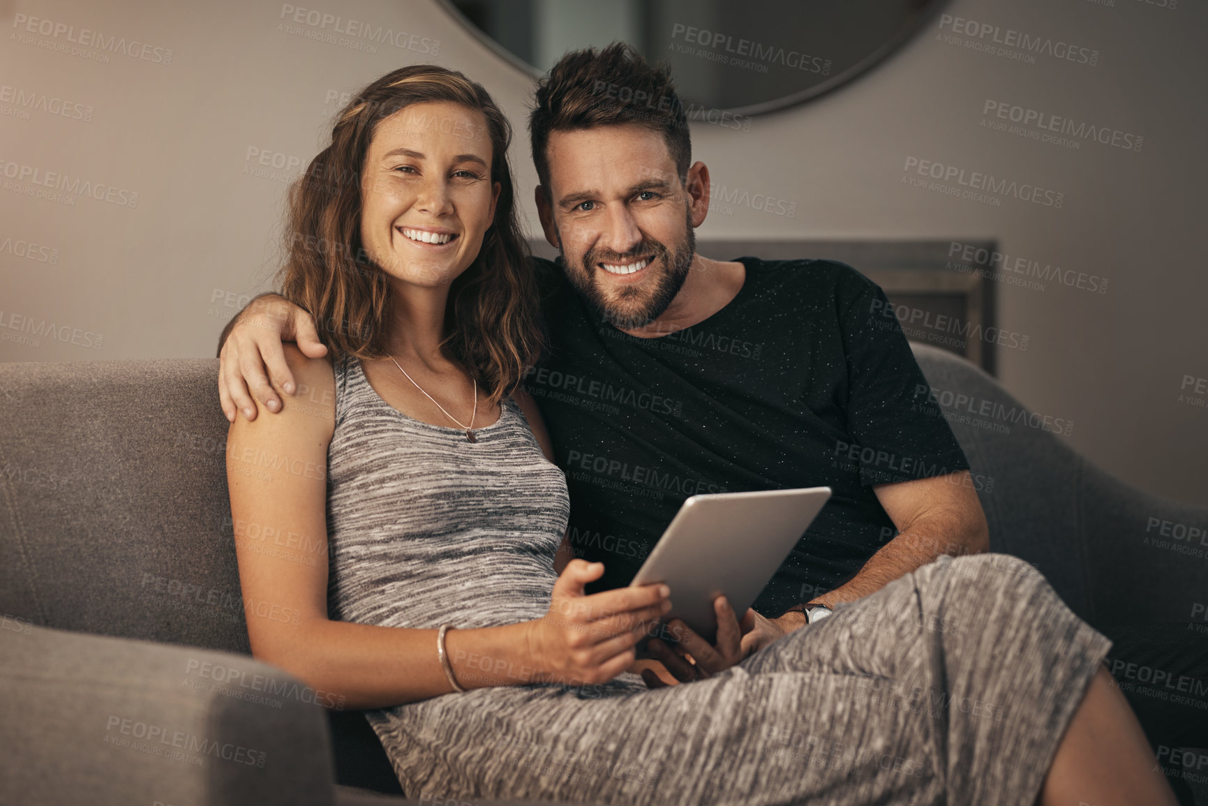 Buy stock photo Portrait of a young couple using a digital tablet together while relaxing on the sofa at home