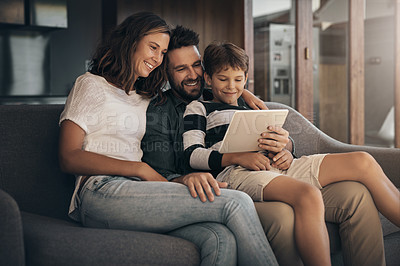 Buy stock photo Shot of an adorable little boy using a digital tablet with his mother and father on the sofa at home