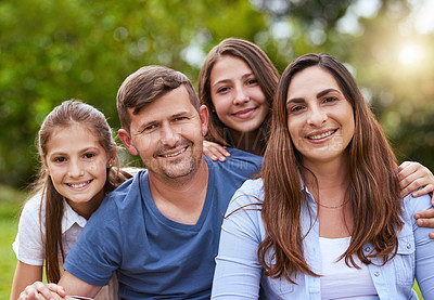 Buy stock photo Portrait of a cheerful young family seated in a park together outside during the day