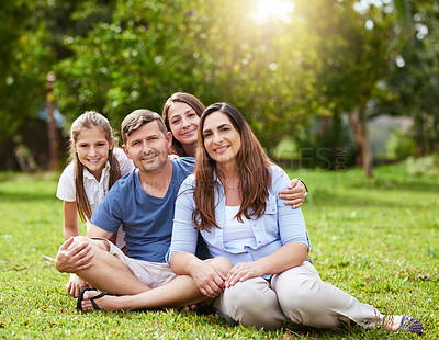 Buy stock photo Portrait of a cheerful young family seated in a park together outside during the day