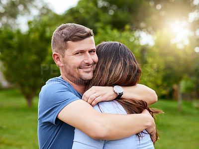 Buy stock photo Portrait of a cheerful young man giving his wife a hug while standing in a park outside during the day