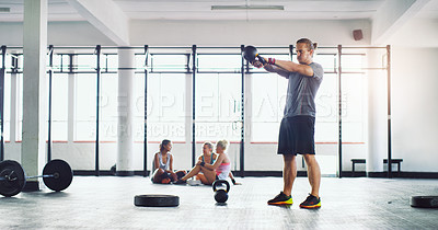 Buy stock photo Shot of a young man working out with kettle bells in a gym