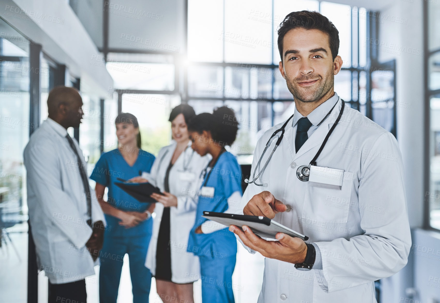 Buy stock photo Portrait of a young doctor using a digital tablet in a hospital with his colleagues in the background