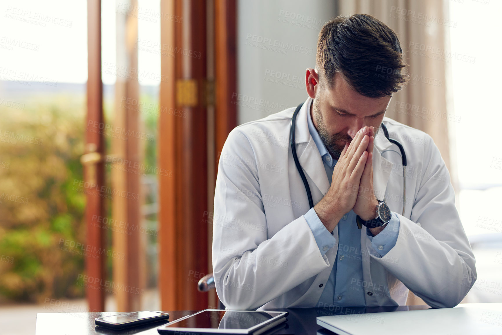 Buy stock photo Cropped shot of a handsome male doctor praying while sitting in his office