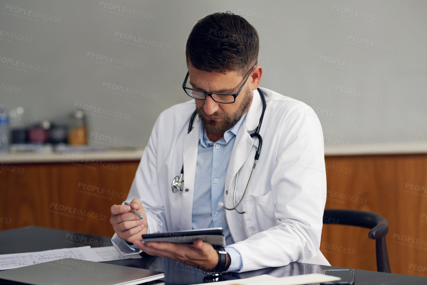 Buy stock photo Cropped shot of a handsome male doctor working on his tablet while sitting in his office
