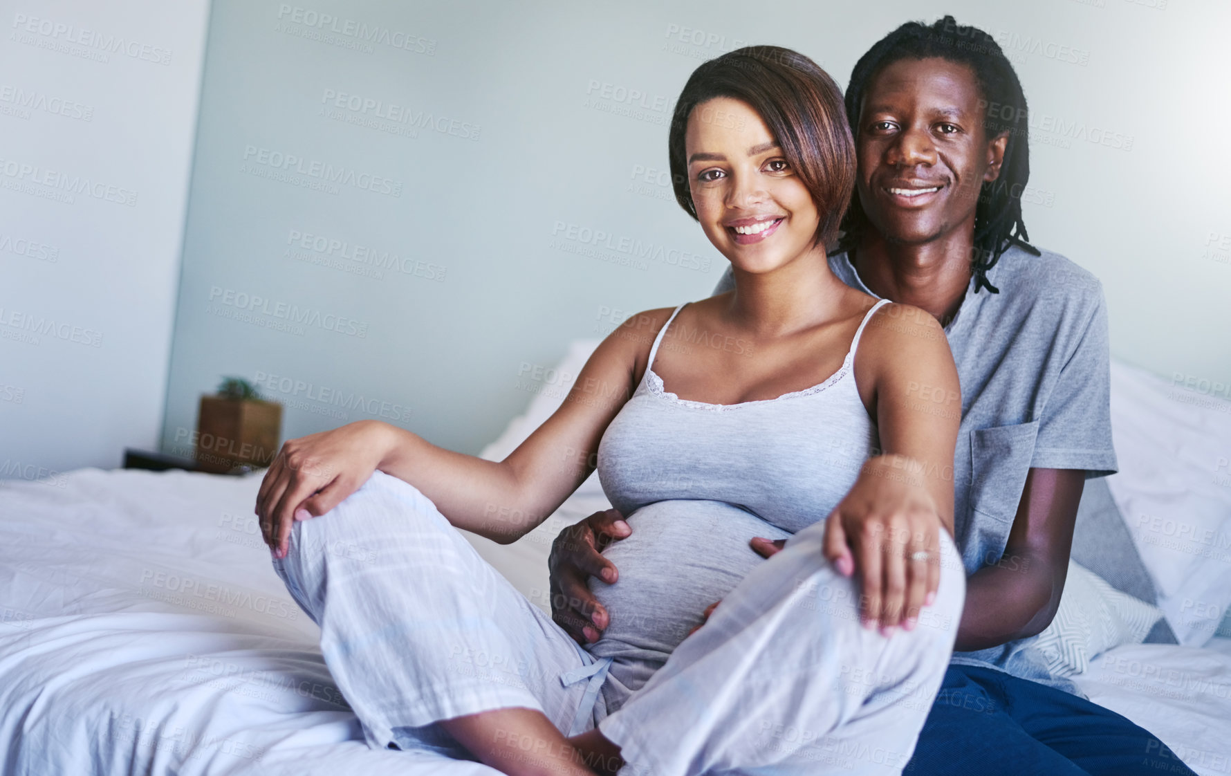 Buy stock photo Shot of a young expecting couple sitting on their bed