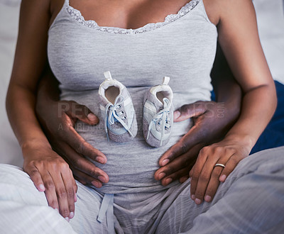 Buy stock photo Shot of a woman with baby shoes on her pregnant belly while sitting with her husband