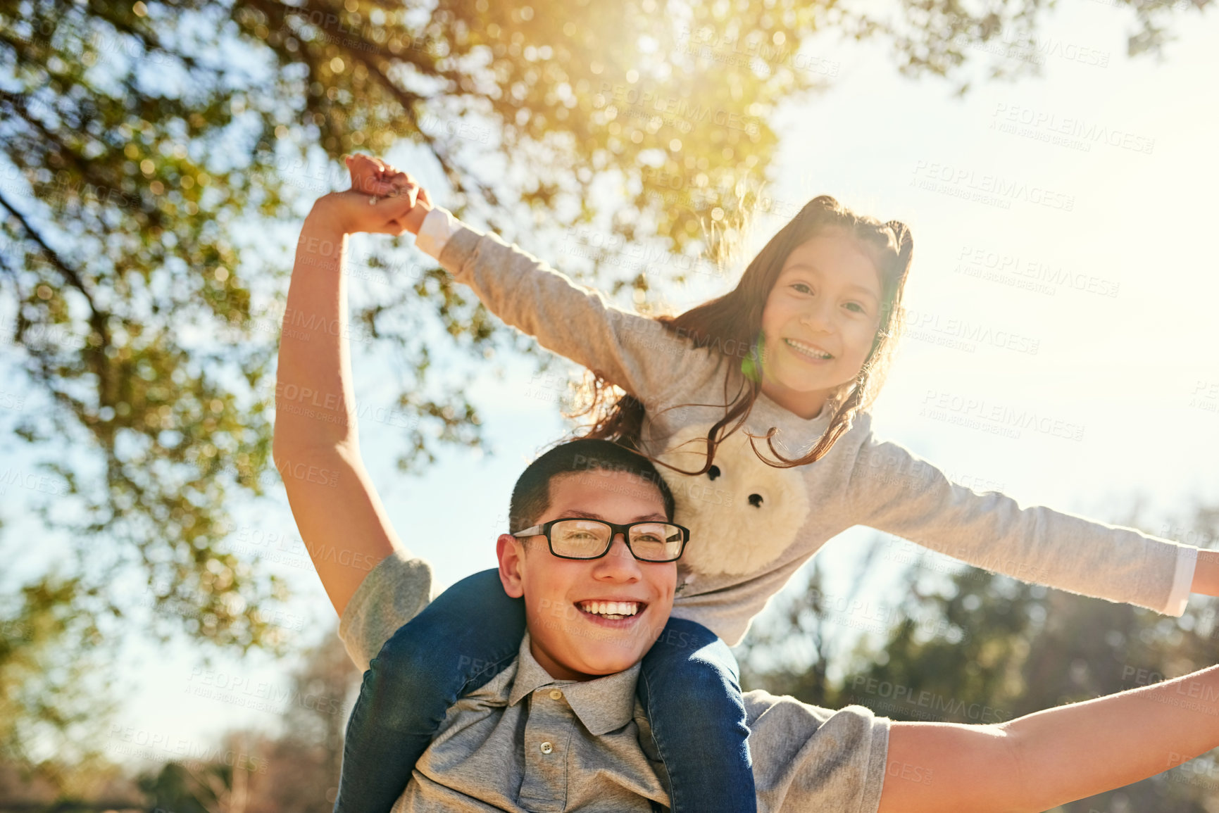 Buy stock photo Low angle shot of a teenage boy carrying his adorable little sister on his shoulders outdoors
