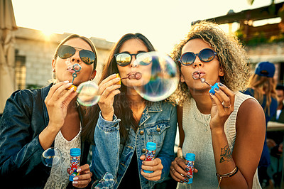 Buy stock photo Shot of a group of young women blowing bubbles together outdoors