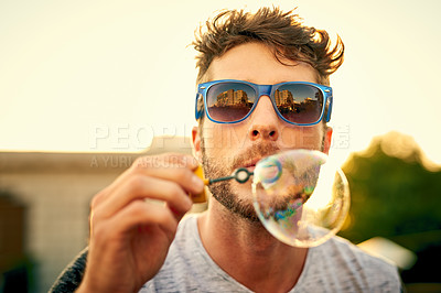 Buy stock photo Shot of a young man blowing bubbles outdoors