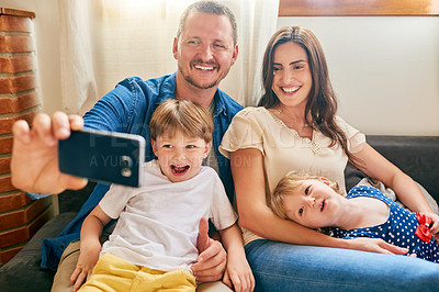 Buy stock photo Shot of a happy young family taking a selfie together on the sofa at home