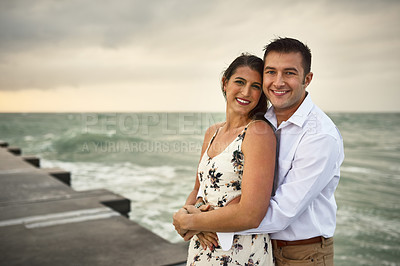 Buy stock photo Cropped portrait of an affectionate young couple standing on the jetty at the beach