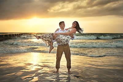 Buy stock photo Full length shot of a handsome young man carrying his girlfriend on the beach