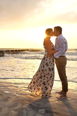 Buy stock photo Couple, kiss and sunset on beach sand, romance and together on vacation for relationship. People, holiday ocean and support for affection in nature, sun flare and honeymoon date on tropical island