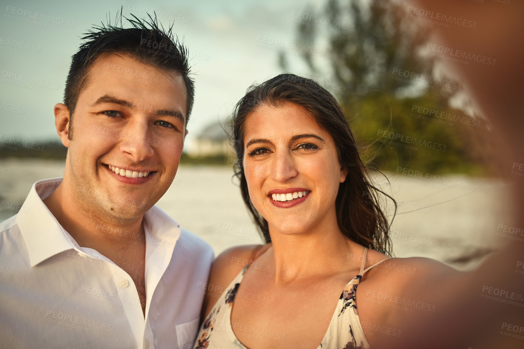 Buy stock photo Cropped portrait of an affectionate young couple taking selfies while standing on the beach