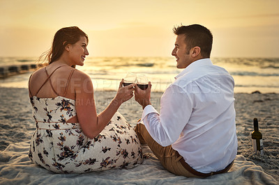 Buy stock photo Rearview shot of an affectionate young couple enjoying some wine while sitting on the beach