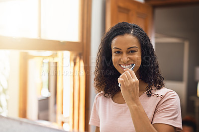 Buy stock photo Cropped portrait of an attractive young woman brushing her teeth in the bathroom at home