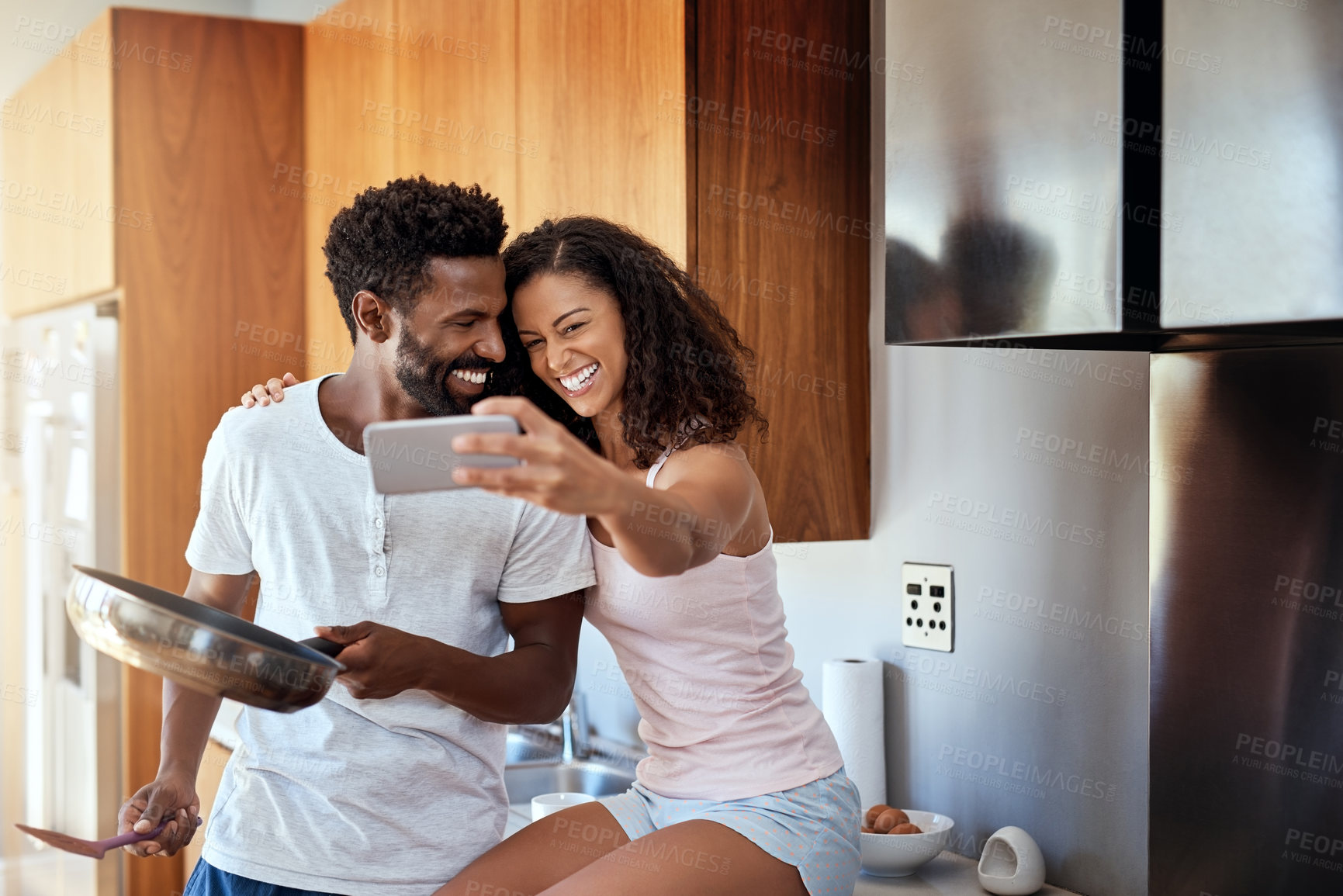 Buy stock photo Cropped shot of an attractive young woman taking selfies of herself and her husband while he cooks in the kitchen
