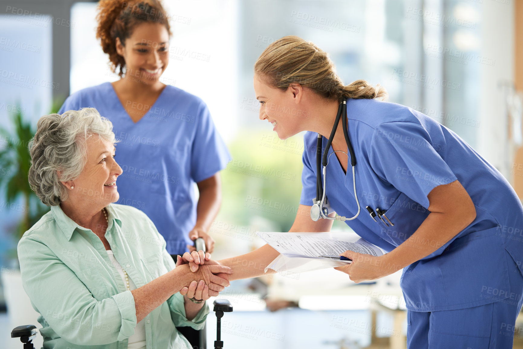 Buy stock photo Shot of an attractive female nurse holding medical records while shaking hands with her wheelchair-bound senior patient in the hospital