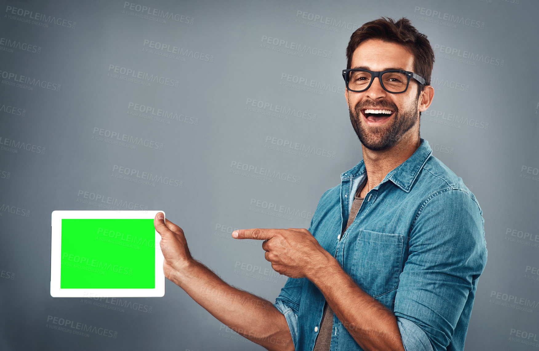 Buy stock photo Happy man, tablet and pointing on mockup green screen for advertising against a grey studio background. Portrait of male person with smile showing technology display, chromakey or copy space branding