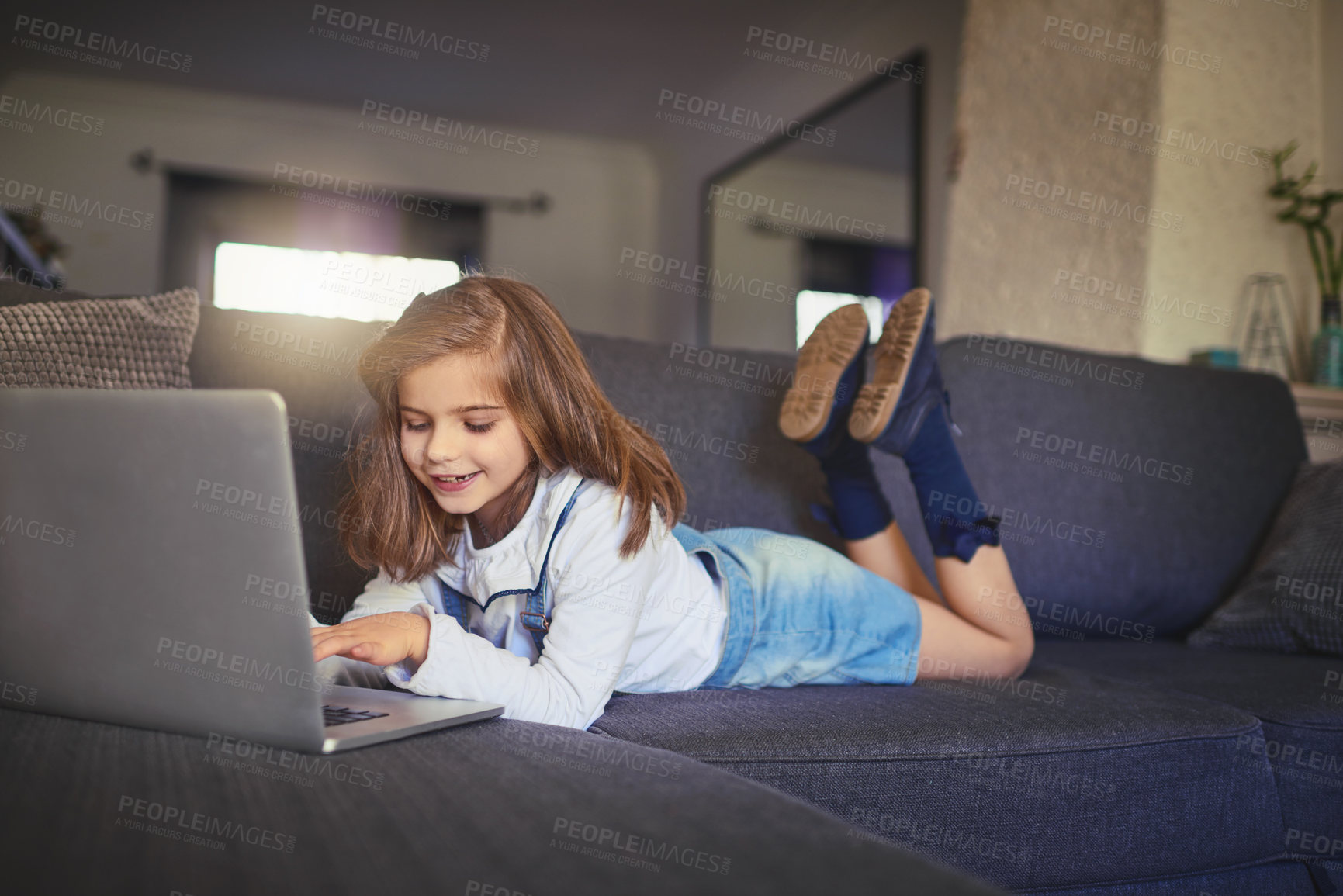 Buy stock photo Laptop, kid and relax on sofa in home for learning, play game or reading ebook online. Computer, child or happy girl lying on couch with internet gaming or streaming video, watch movie or cartoon