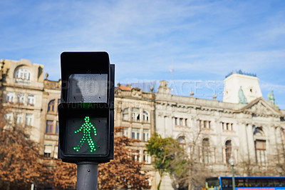 Buy stock photo Shot of a pedestrian traffic light with city buildings situated in the background outside during the day