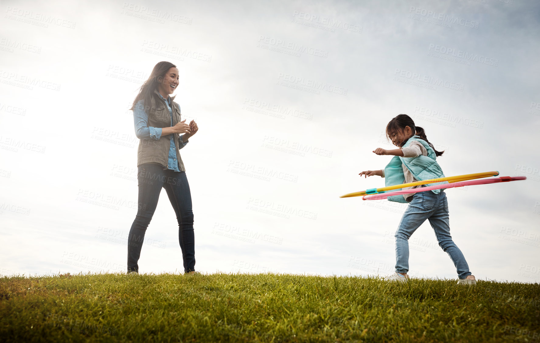 Buy stock photo Shot of a mother watching her daughter spinning the hula hoop