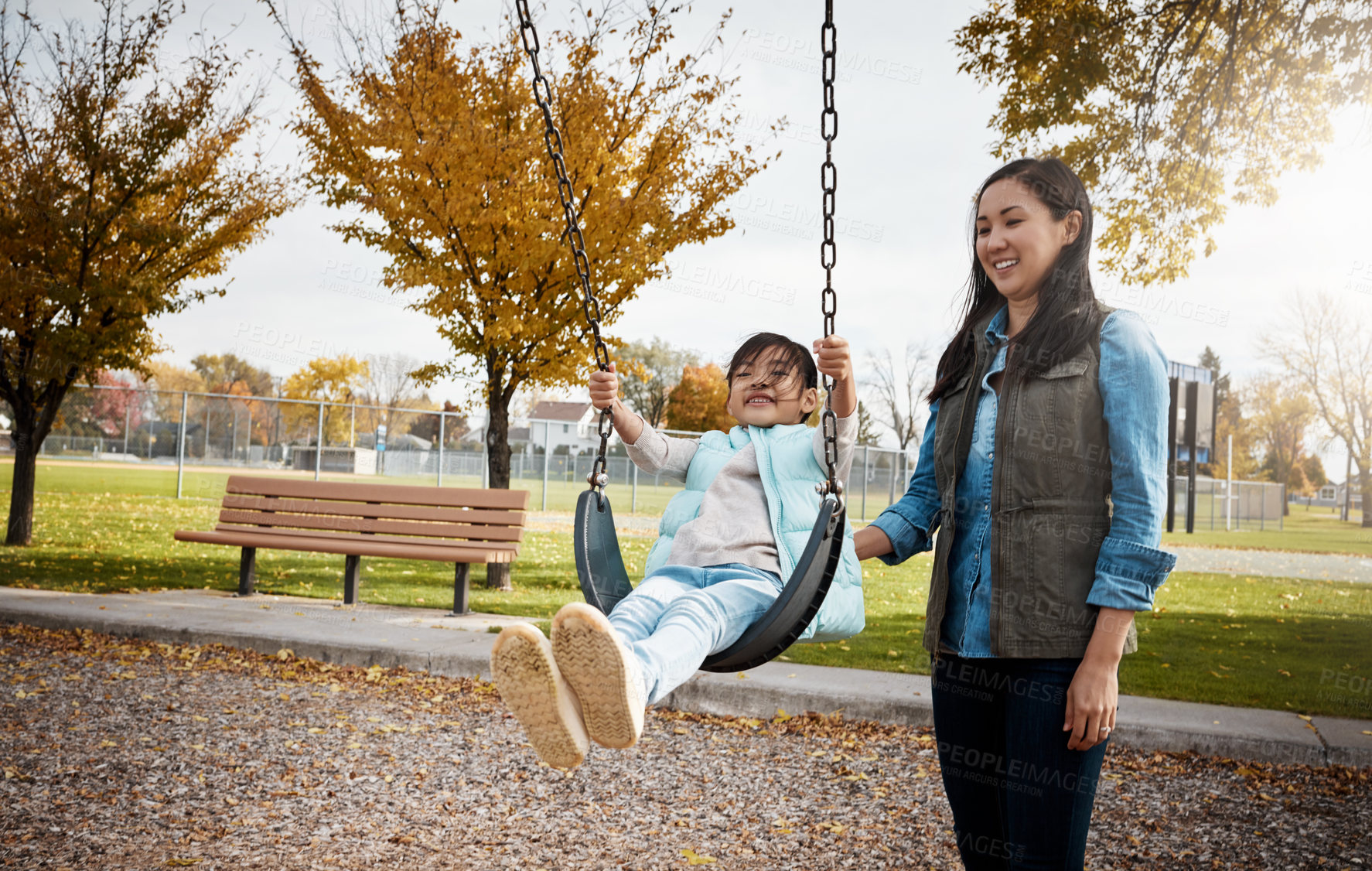Buy stock photo Shot of a mother pushing her little daughter on a swing at the park