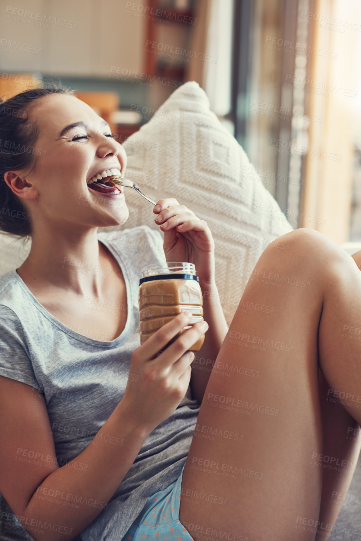 Buy stock photo Shot of an attractive young woman eating peanut butter while relaxing on the sofa at home