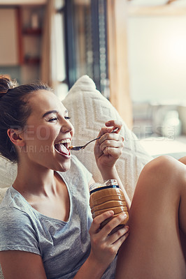 Buy stock photo Shot of an attractive young woman eating peanut butter while relaxing on the sofa at home