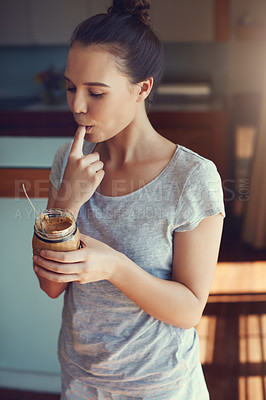 Buy stock photo Shot of an attractive young woman eating peanut butter while standing in the kitchen at home