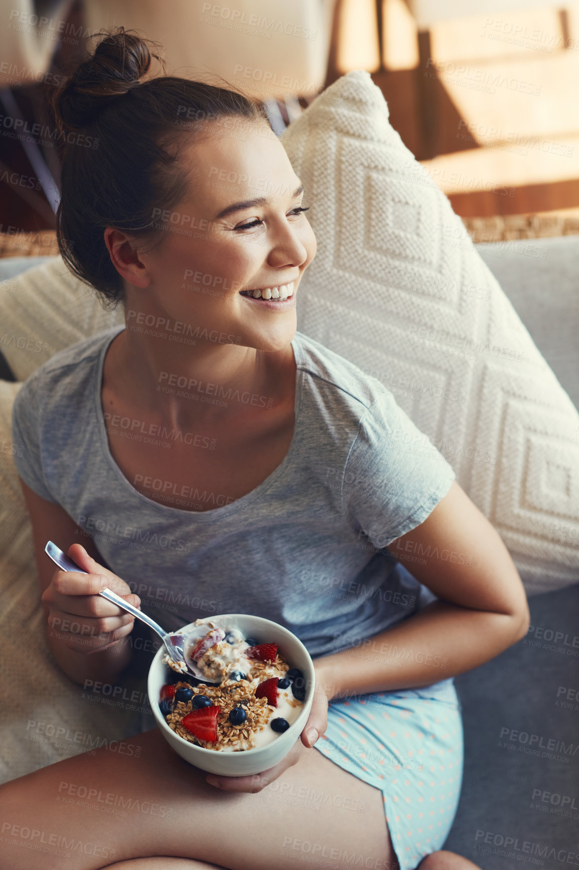 Buy stock photo Shot of an attractive young woman eating her breakfast while relaxing on the sofa at home