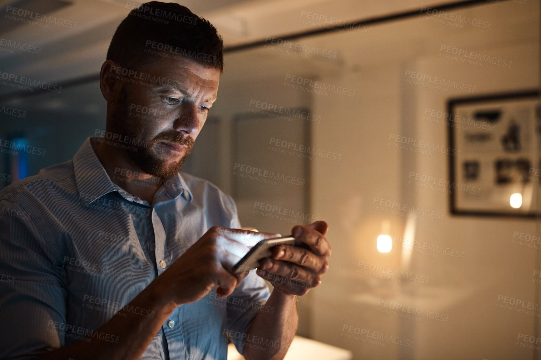 Buy stock photo Shot of a mature businessman using a cellphone while working late in an office