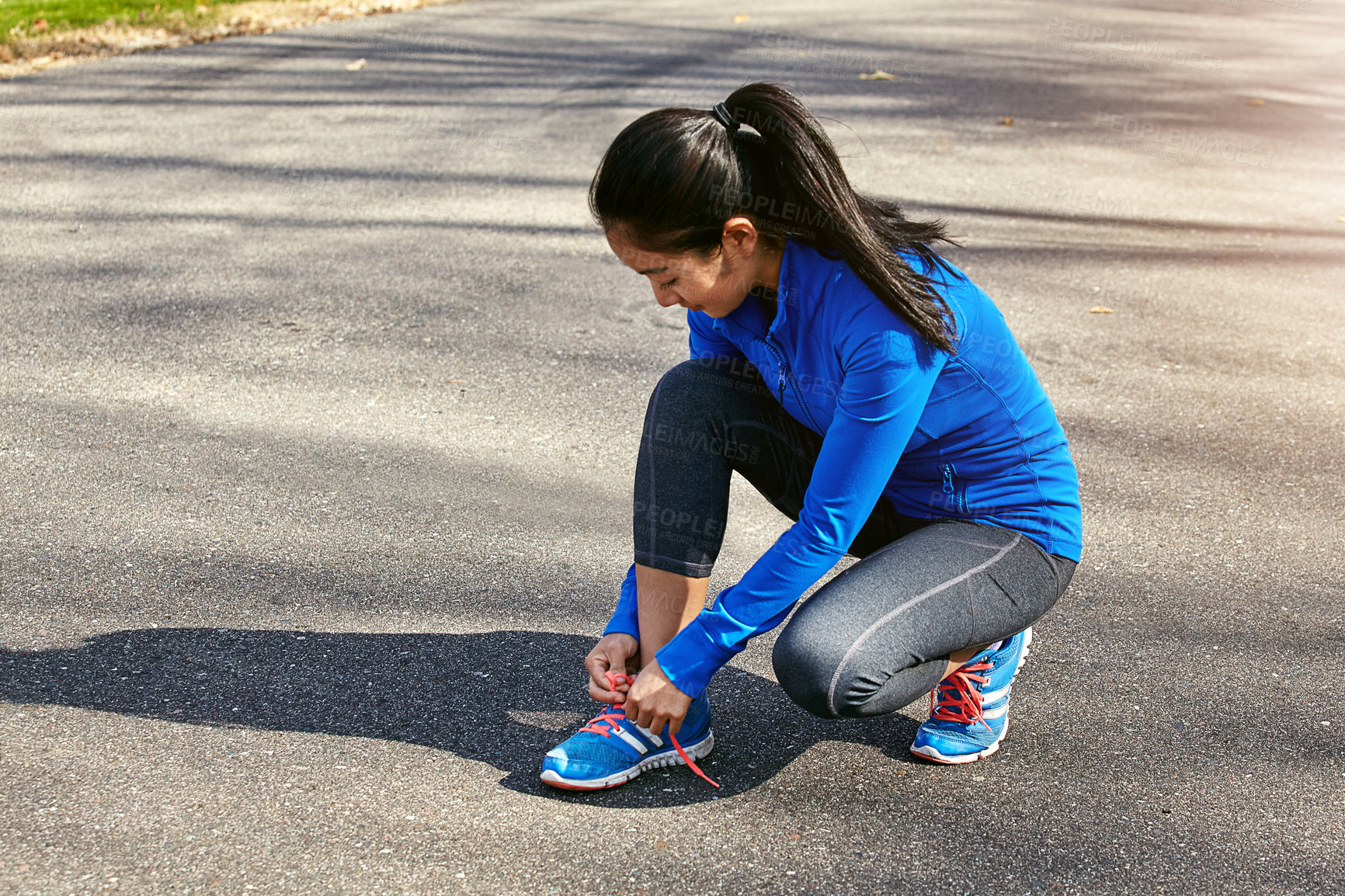 Buy stock photo Shot of a sporty young woman tying her shoelaces while exercising outdoors