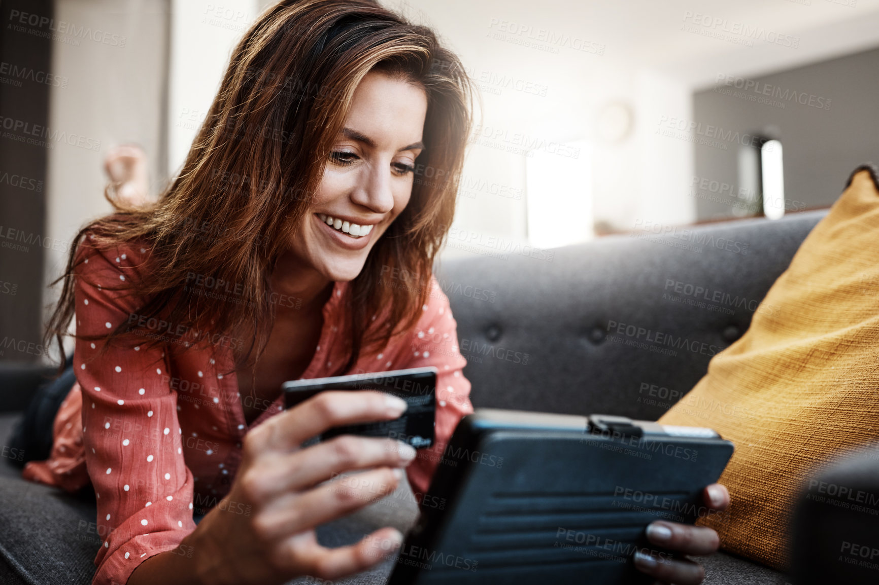 Buy stock photo Shot of an attractive young woman using a digital tablet and credit card on the sofa at home