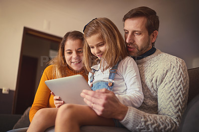 Buy stock photo Cropped shot of an affectionate young family of three using a digital tablet while sitting on the sofa at home