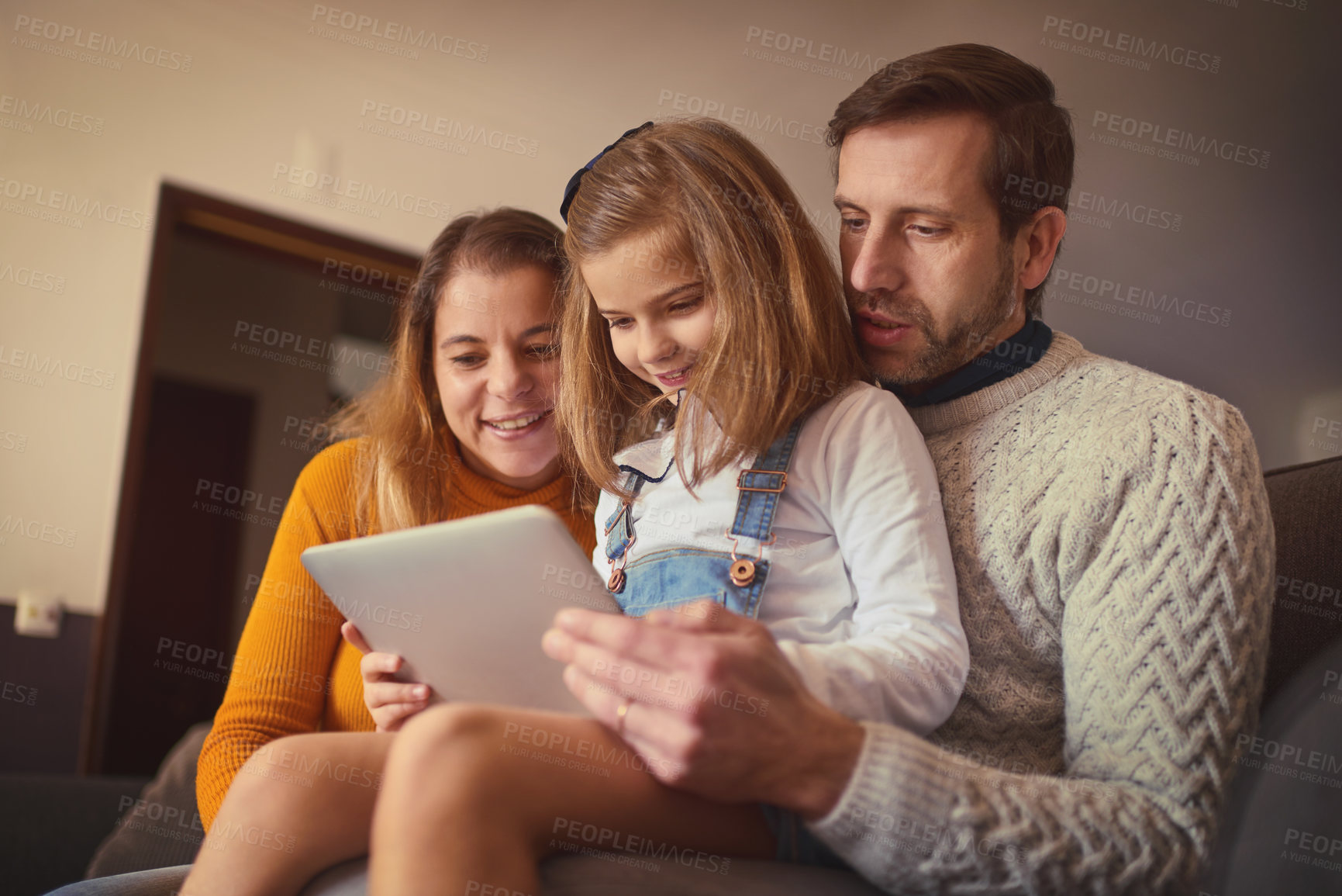 Buy stock photo Cropped shot of an affectionate young family of three using a digital tablet while sitting on the sofa at home