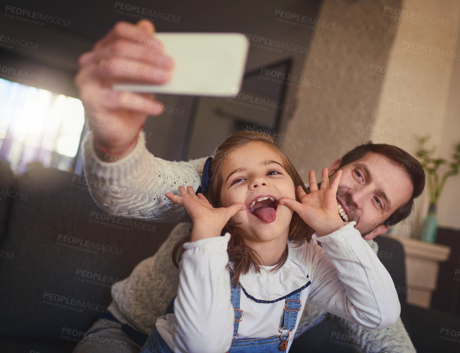 Buy stock photo Cropped shot of a handsome man and his adorable young daughter taking selfies on the sofa at home